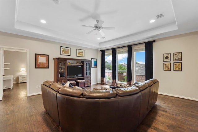 living area with dark wood-style flooring, a raised ceiling, visible vents, ceiling fan, and baseboards