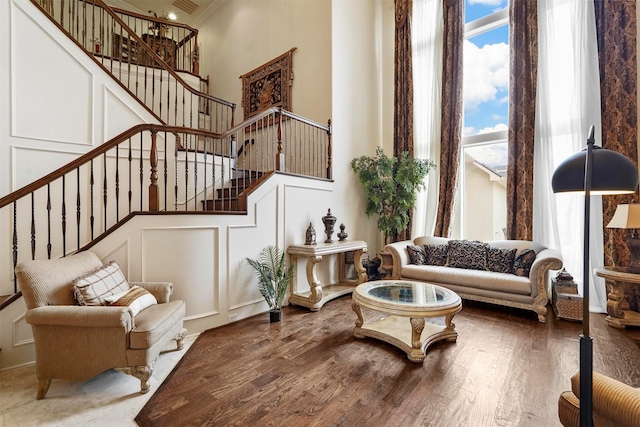 living area featuring crown molding, a decorative wall, a high ceiling, wood finished floors, and stairs