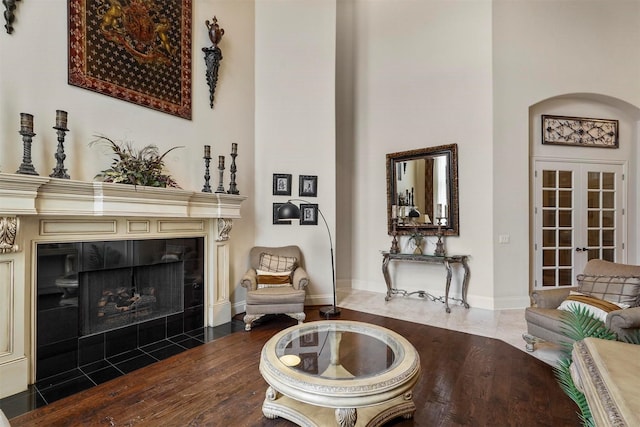 sitting room with baseboards, a towering ceiling, wood finished floors, french doors, and a fireplace