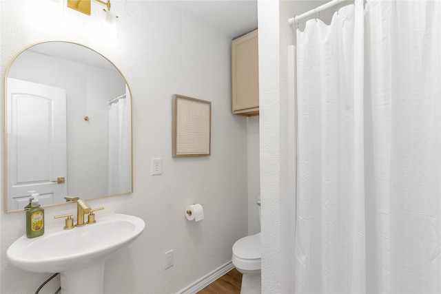 bathroom with toilet, a shower with shower curtain, wood finished floors, a sink, and baseboards