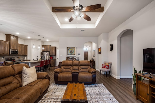 living room with baseboards, visible vents, arched walkways, a raised ceiling, and dark wood-style flooring