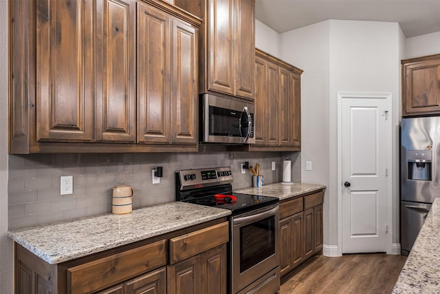 kitchen with appliances with stainless steel finishes, dark wood-style flooring, backsplash, and light stone counters