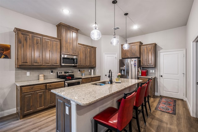 kitchen featuring decorative backsplash, appliances with stainless steel finishes, wood finished floors, light stone countertops, and a sink