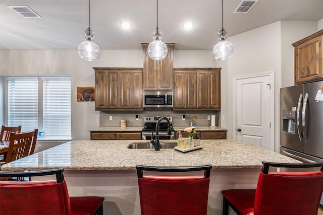 kitchen with stainless steel appliances, visible vents, hanging light fixtures, a sink, and an island with sink