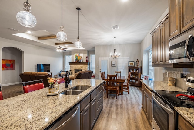 kitchen with a stone fireplace, light wood-style flooring, stainless steel appliances, a sink, and decorative backsplash