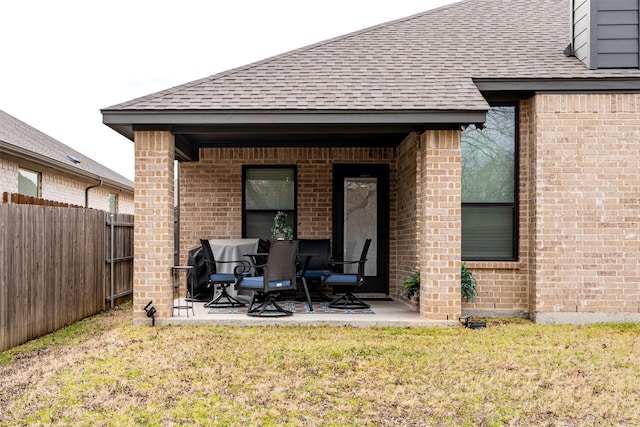 rear view of house featuring roof with shingles, a lawn, a patio, and fence