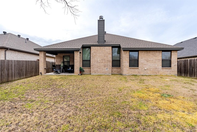 back of house with a fenced backyard, a chimney, a yard, a patio area, and brick siding