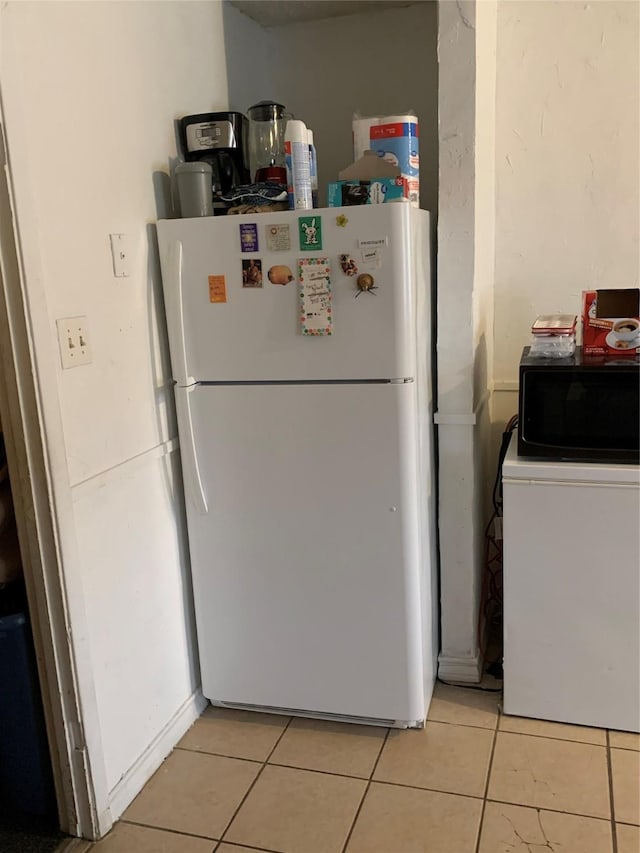 kitchen featuring freestanding refrigerator, black microwave, and light tile patterned floors