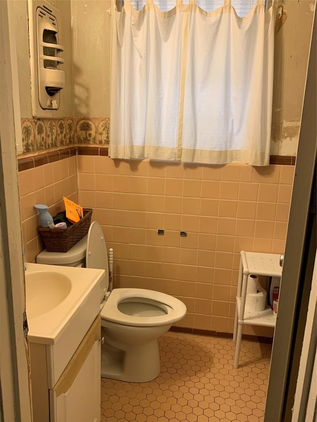 half bathroom featuring tile patterned flooring, toilet, vanity, wainscoting, and wallpapered walls