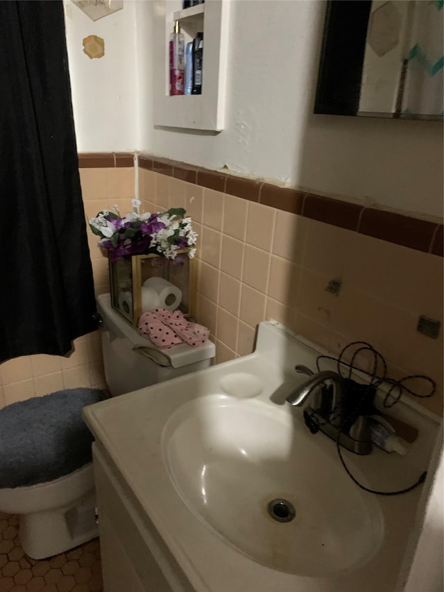 bathroom with tile walls, toilet, wainscoting, a sink, and tile patterned floors