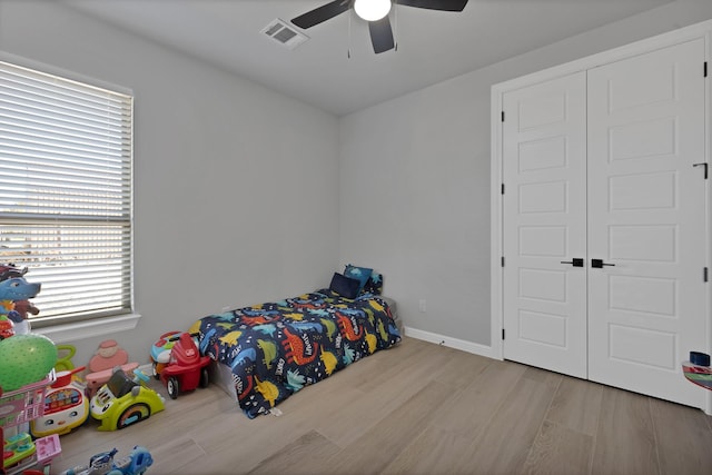 bedroom with baseboards, visible vents, ceiling fan, wood finished floors, and a closet