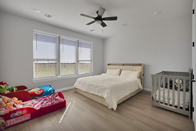 bedroom with ceiling fan, wood finished floors, visible vents, and baseboards