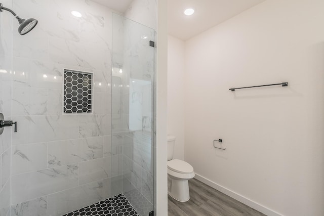 bathroom featuring toilet, a marble finish shower, baseboards, and wood finished floors