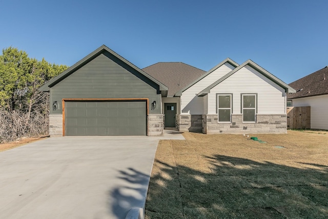 craftsman-style house featuring a garage, driveway, stone siding, and a front yard