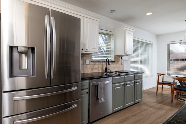 kitchen featuring dark countertops, wood finished floors, a sink, stainless steel appliances, and backsplash