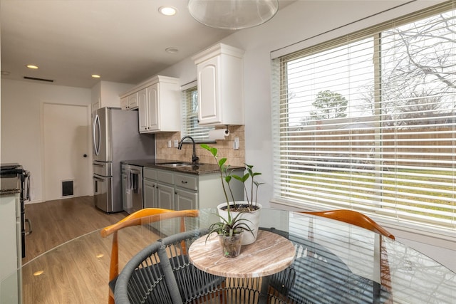 kitchen featuring tasteful backsplash, wood finished floors, a sink, white cabinetry, and stainless steel dishwasher