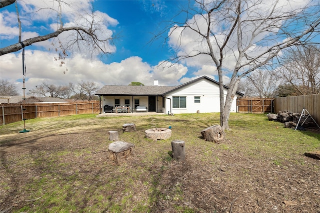 rear view of house featuring a patio, a chimney, a lawn, a fenced backyard, and a fire pit