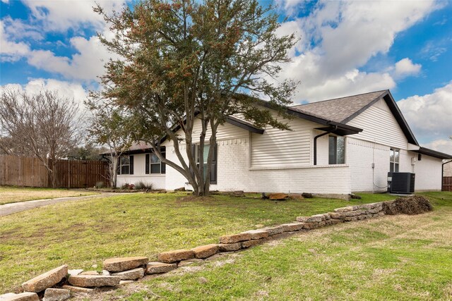 view of property exterior with cooling unit, brick siding, a shingled roof, fence, and a lawn