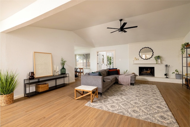 living area with a fireplace, a ceiling fan, vaulted ceiling, and wood finished floors