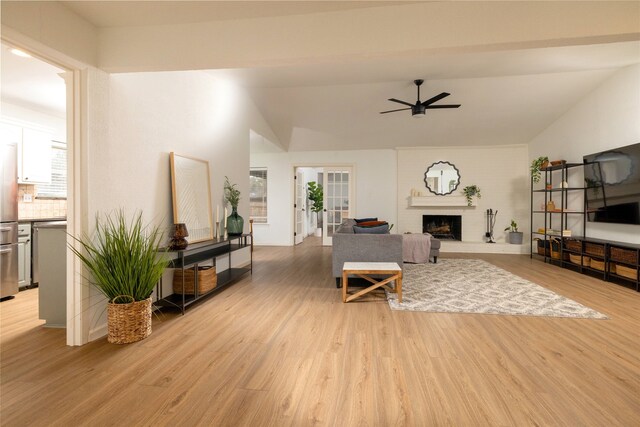 living area featuring light wood-type flooring, a fireplace, vaulted ceiling, and a ceiling fan