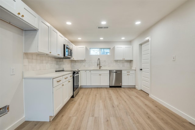 kitchen with light countertops, backsplash, appliances with stainless steel finishes, white cabinets, and a sink