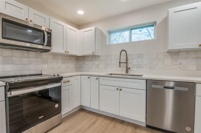 kitchen with appliances with stainless steel finishes, light countertops, a sink, and white cabinetry