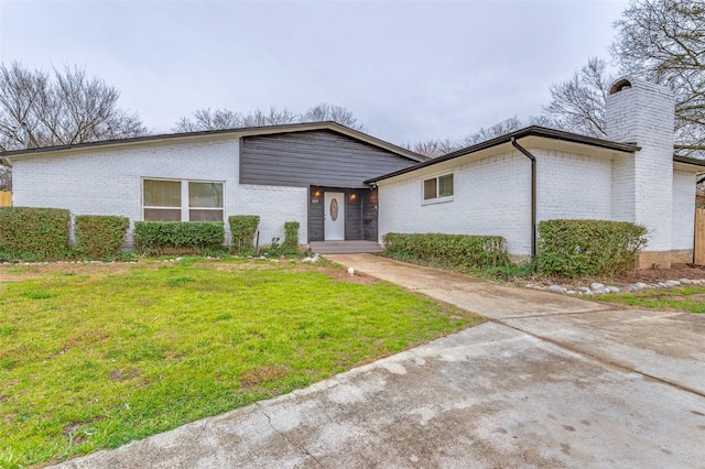 mid-century modern home featuring a front yard, brick siding, and a chimney