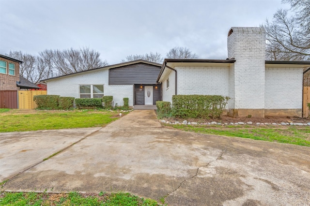 mid-century modern home featuring brick siding, a front lawn, fence, and a chimney
