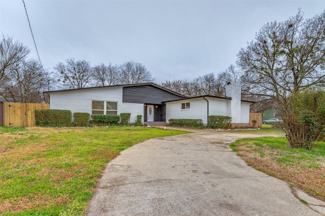 mid-century modern home with a chimney, driveway, a front lawn, brick siding, and fence