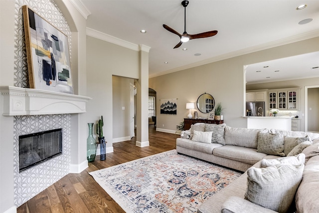 living room with ornamental molding, a tile fireplace, baseboards, and wood finished floors