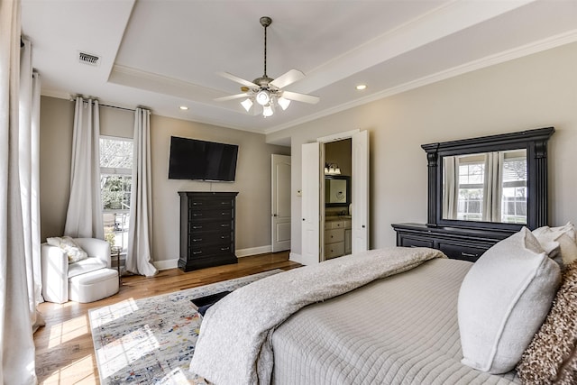 bedroom featuring wood finished floors, visible vents, baseboards, ornamental molding, and a raised ceiling