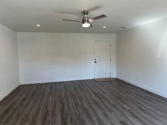 empty room with a textured ceiling, dark wood finished floors, a ceiling fan, and baseboards