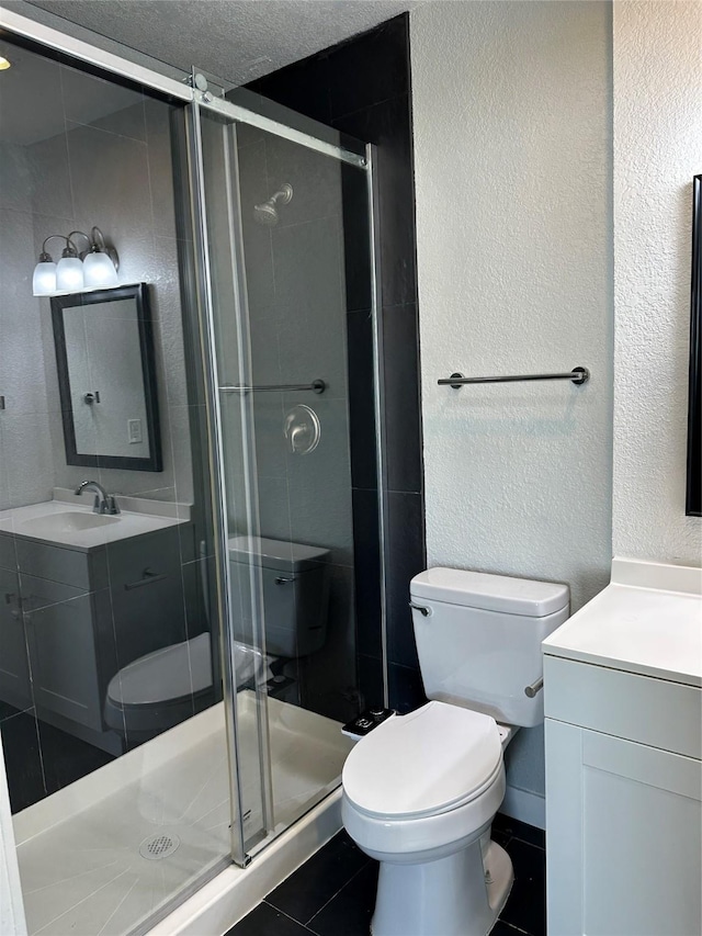 bathroom featuring a textured wall, toilet, vanity, a shower stall, and tile patterned floors