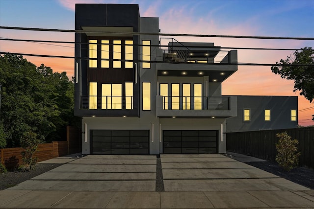 contemporary home featuring stucco siding, an attached garage, fence, a balcony, and driveway