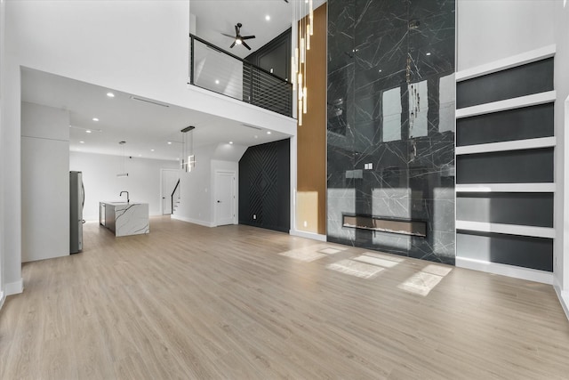 unfurnished living room with recessed lighting, stairway, a towering ceiling, a ceiling fan, and light wood-type flooring