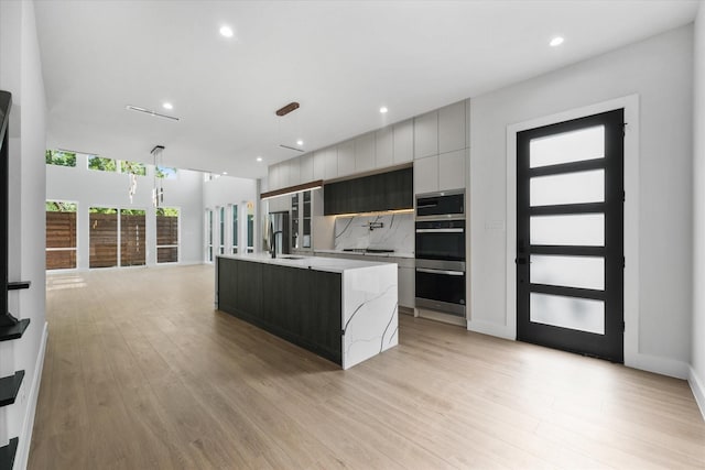 kitchen featuring modern cabinets, a sink, double wall oven, light wood-style floors, and backsplash