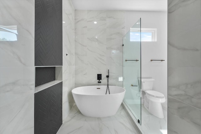 bathroom featuring toilet, marble finish floor, a soaking tub, and tile walls