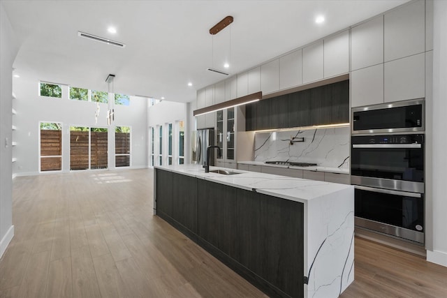 kitchen featuring tasteful backsplash, appliances with stainless steel finishes, a kitchen island with sink, a sink, and modern cabinets