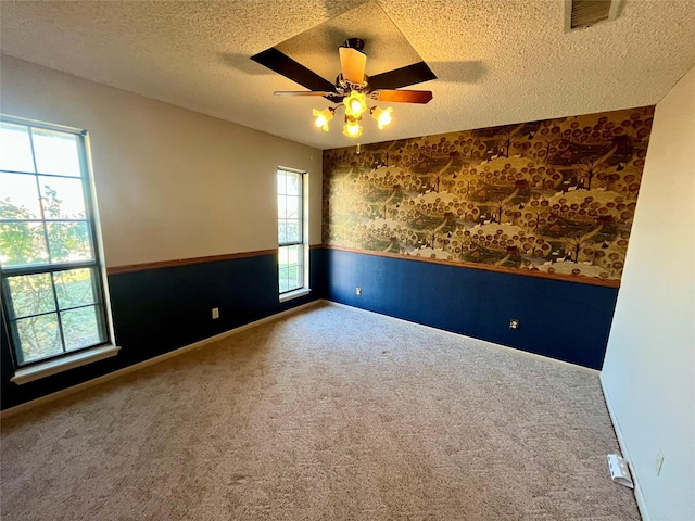 empty room featuring a wainscoted wall, visible vents, a textured ceiling, carpet floors, and wallpapered walls