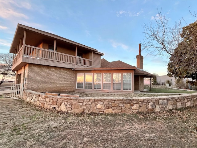 rear view of house featuring a balcony, brick siding, and a chimney