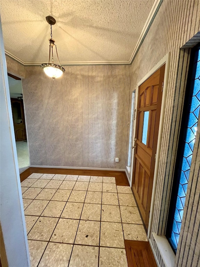 foyer entrance with a textured ceiling, ornamental molding, and light tile patterned flooring