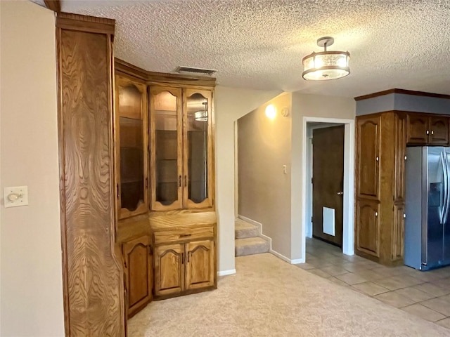 corridor with visible vents, a textured ceiling, light tile patterned floors, light colored carpet, and stairs