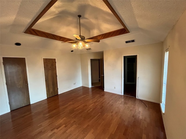 unfurnished bedroom featuring visible vents, a raised ceiling, a textured ceiling, and dark wood-style floors