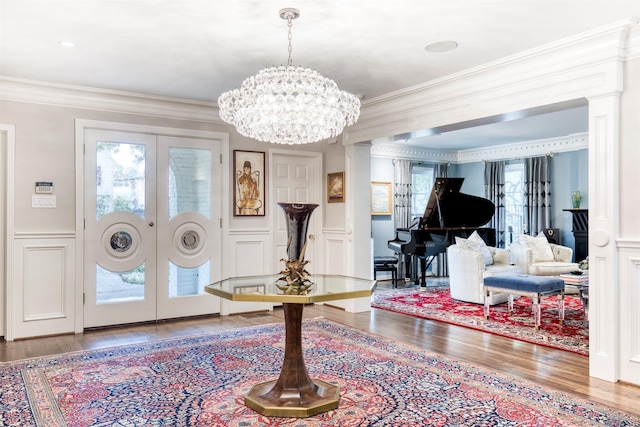 foyer with ornamental molding, a decorative wall, wood finished floors, and french doors