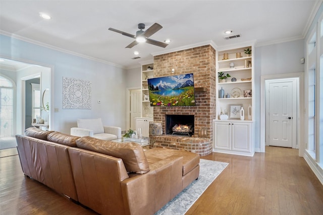 living room featuring built in shelves, wood finished floors, visible vents, a brick fireplace, and crown molding