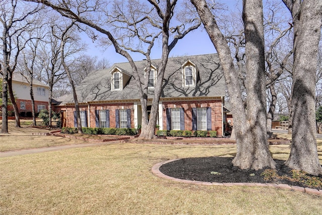 cape cod home featuring roof with shingles, brick siding, and a front lawn