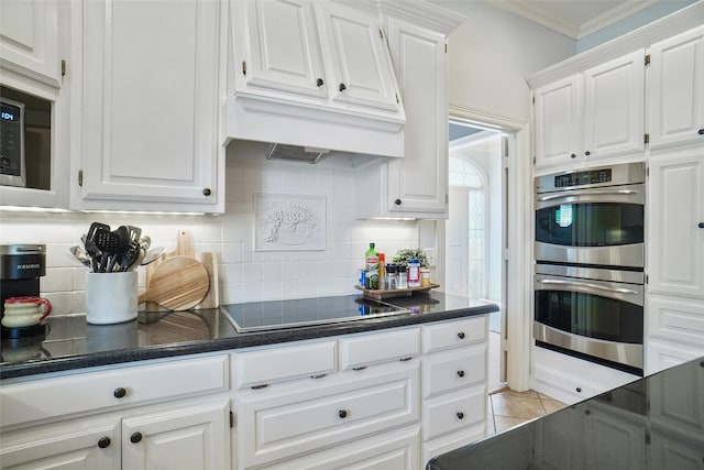 kitchen with stainless steel appliances, ornamental molding, dark countertops, and white cabinetry