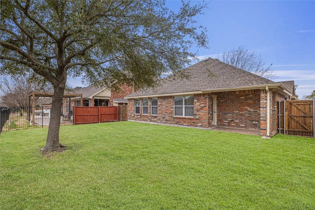 rear view of property with roof with shingles, brick siding, a lawn, and a fenced backyard