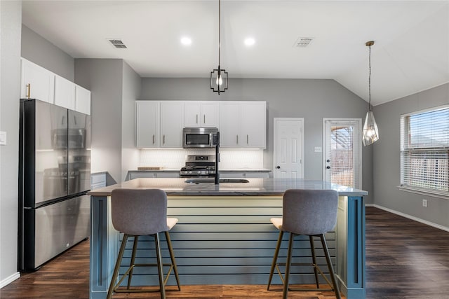 kitchen with visible vents, a center island with sink, appliances with stainless steel finishes, and decorative backsplash