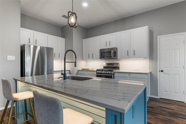 kitchen featuring light stone counters, a sink, appliances with stainless steel finishes, decorative backsplash, and a center island with sink